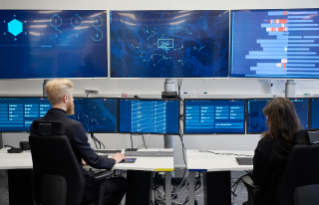 Two persons in front of several big screens