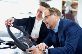 A woman and a man holding in and discussing a steering wheel 